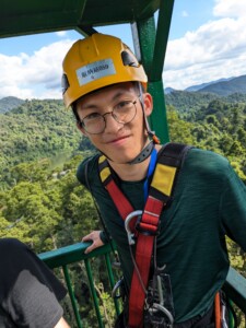 Photo of a man wearing a hard hat and harness with forested hills in the background.