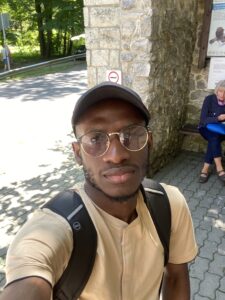 Photograph of the head and shoulders of a man standing in front of a wall and road.