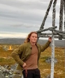 Photograph of a man standing in front of an upland hillside.