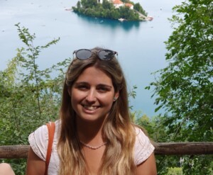 Photograph of a woman, with trees and an expanse of water in the background.