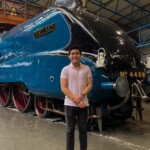 Photograph of a man standing in front of a historic steam locomotive.