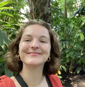 Photo of a woman with tropical foliage in the background.