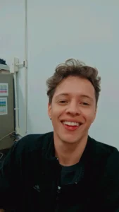 A photograph of the head and shoulders of a smiling man in an office environment.