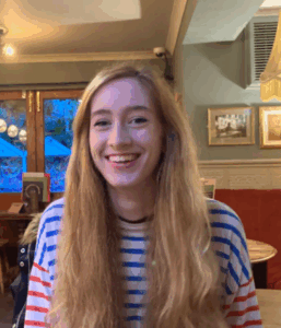 A photograph of a woman seated in an indoors bar or restaurant environment.
