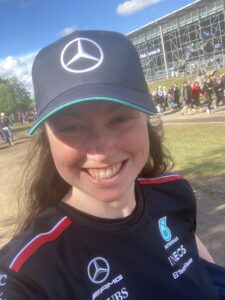 A photograph of a woman standing in front of a stand at a racing circuit.