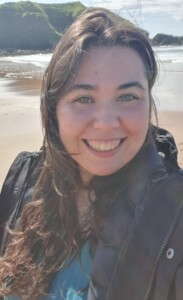 A photograph of the head and shoulders of a woman with a beach in the background.