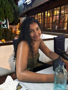 Photograph of a woman seated at a table outside a bar or cafe.