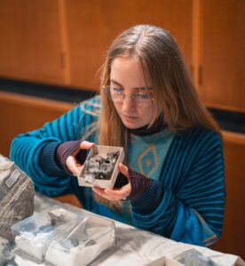 Photo of a seated woman examining a fossil specimen in a box.