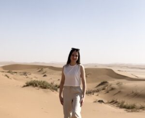 Photo of a woman standing in front of a desert landscape of extensive sand dunes.