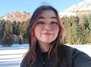 Photograph of the head and shoulders of a woman standing in front of a snowy and forested mountainous background.