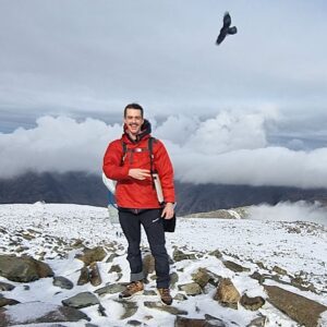 A photo of a man standing on a snowy mountain with a bird flying overhead.