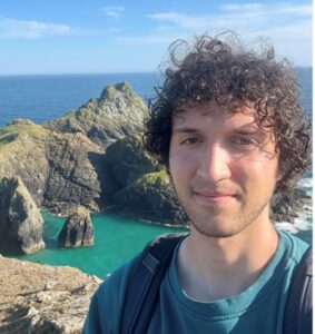 Photo of the head and shoulders of a man standing in front of a rocky coast.