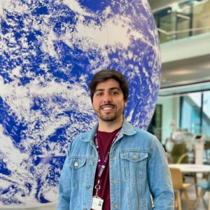 A photo of the upper body of a man standing in front of a large globe.