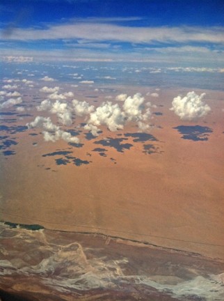 Scattering clouds casting shadows on a barren landscape, seen from above to illustrate the clear-sky bias of satellites.
