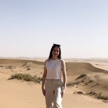 Photo of a woman standing in front of a desert landscape of extensive sand dunes.