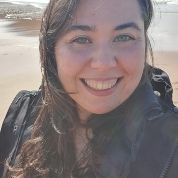 A photograph of the head and shoulders of a woman with a beach in the background.