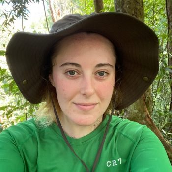 A photo of the head and shoulders of a woman in front of a wooded backdrop.