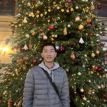 A photo of a man standing in front of a Christmas tree.
