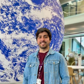 A photo of the upper body of a man standing in front of a large globe.