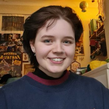 Head and shoulders photo of a woman, with a wall with posters behind.