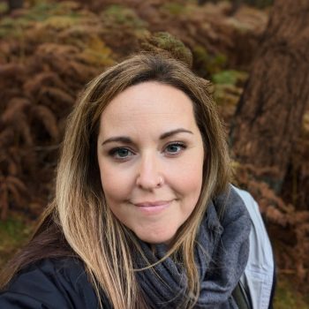 Head and shoulders photograph of a woman with a tree and bracken in the background.
