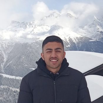 A photo of the head and upper body of a man standing in front of a snowy, mountainous landscape.