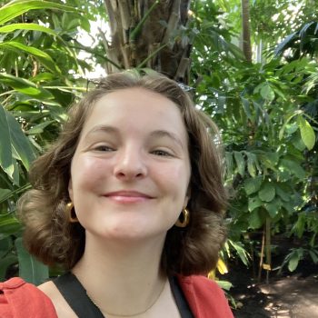 Photo of a woman with tropical foliage in the background.