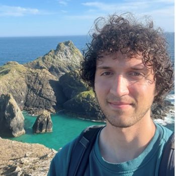 Photo of the head and shoulders of a man standing in front of a rocky coast.